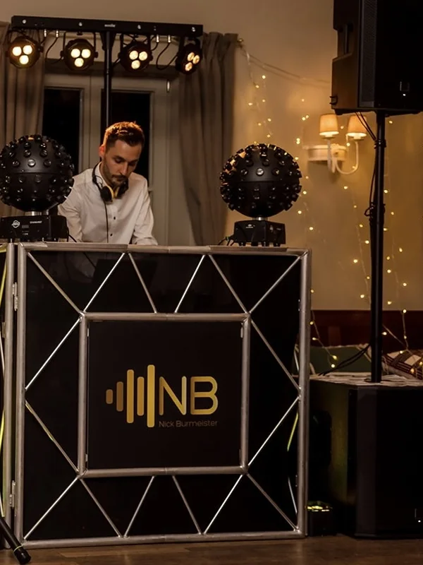 Nick Burmeister DJing at a wedding reception, warm string lights in the background